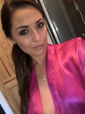 Femme aux gros seins en robe de nuit en satin rose posant nue devant un miroir